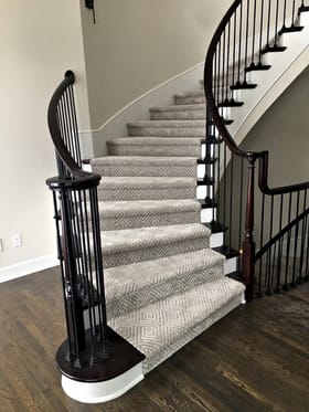 Curved staircase with diamond-pattern stair carpet and black iron balusters