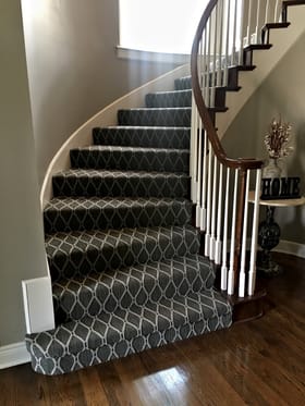 Curved staircase with grey lattice-pattern stair carpet and white balusters