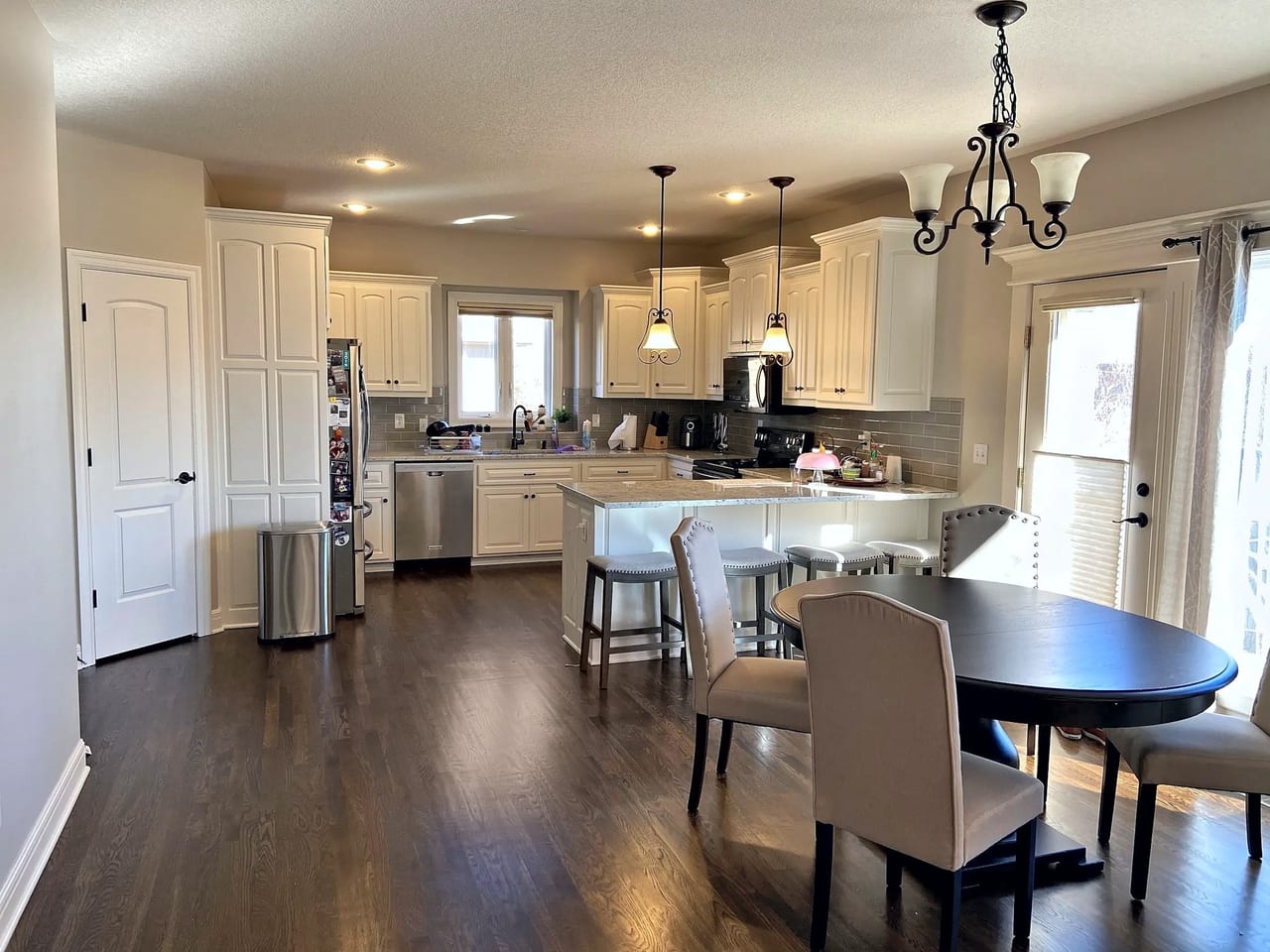 Kitchen and dining area with refinished dark hardwood floors, cream cabinets, an island with stools, and a round table by the patio door