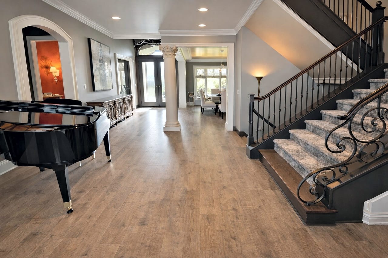 Refinished maple floor in the front hall of a Kansas City metro home, with a grand piano and a carpeted staircase.
