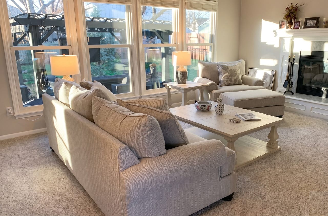 Living room with wall-to-wall carpet in a light grey twist, sofa and fireplace in afternoon sun